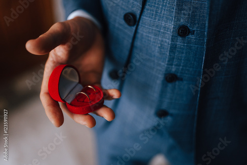 The groom in a suit holds wedding rings in his hand