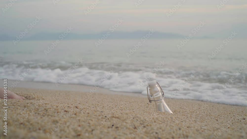 A barefoot woman discovers a drifting bottle with a rolled-up message on the sandy beach. She picks it up as gentle waves touch her feet, evoking a sense of mystery and connection.