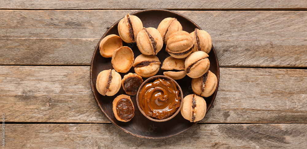 Plate with sweet walnut shaped cookies with boiled condensed milk on wooden background Plate with sweet walnut shaped cookies with boiled condensed milk on wooden background