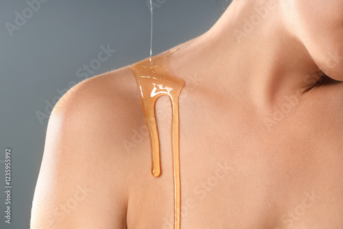 Photos Young woman with dripping honey on collarbone against grey background, closeup