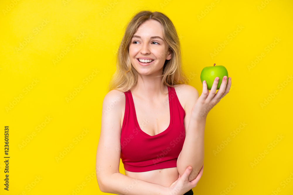 Blonde English young girl isolated on yellow background with an apple and happy Blonde English young girl isolated on yellow background with an apple and happy