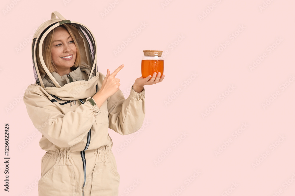 Female beekeeper pointing at jar of sweet honey on pink background Female beekeeper pointing at jar of sweet honey on pink background