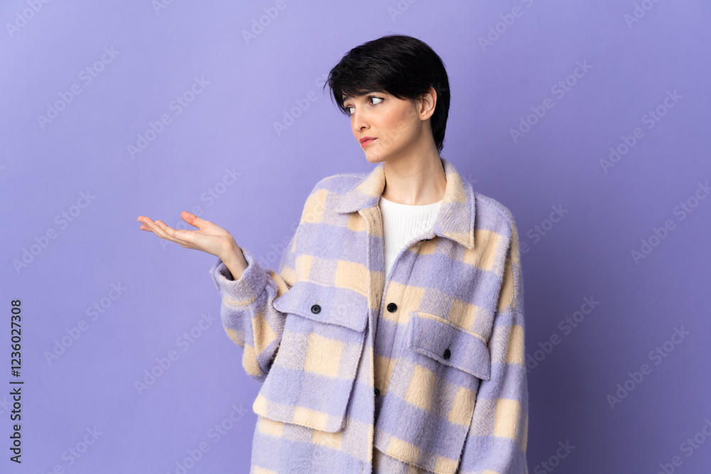 Woman with short hair isolated on purple background holding copyspace with doubts Woman with short hair isolated on purple background holding copyspace with doubts