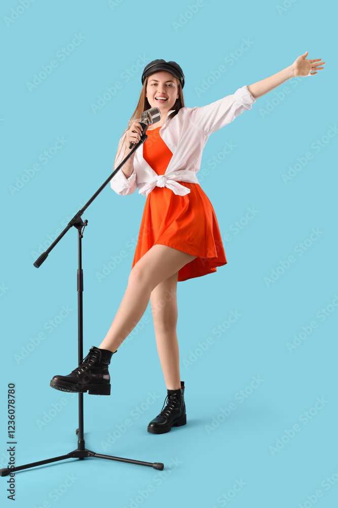 Fototapeta premium Young woman with microphone singing karaoke on blue background