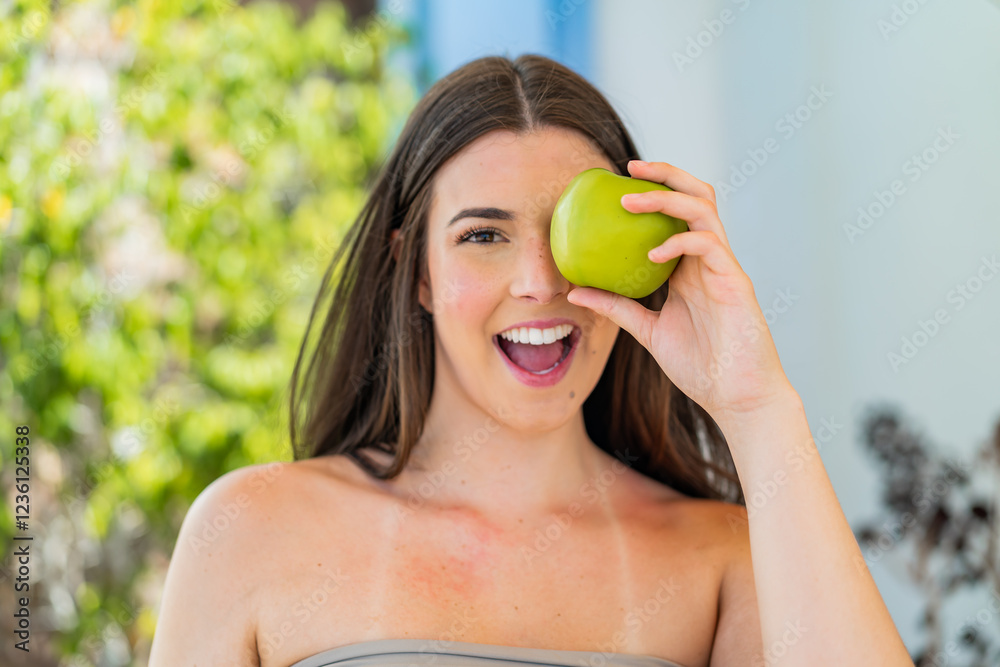 Young pretty Brazilian woman at outdoors holding an apple with surprised expression Young pretty Brazilian woman at outdoors holding an apple with surprised expression