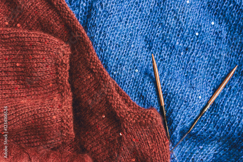 Obraz na płótnie Red and blue knitted sweater with sequins and knitting needles. Sequinned knitwear on wooden needles. Sequin pattern in needlework. Knitting hobby. Knitter work. Sequins texture in knitwear. w salonie