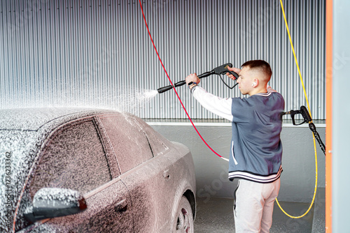 A man applies foam to a car to remove dirt at a car wash.