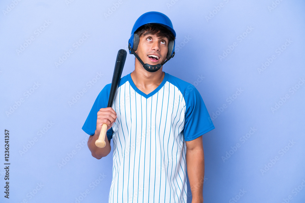 Baseball caucasian man player with helmet and bat isolated on blue background looking up and with surprised expression Baseball caucasian man player with helmet and bat isolated on blue background looking up and with surprised expression