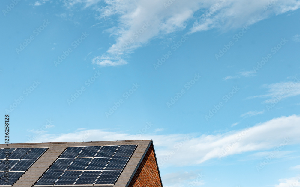 Fototapeta premium Solar panels installed on a modern building roof under a clear blue sky with scattered clouds during the day