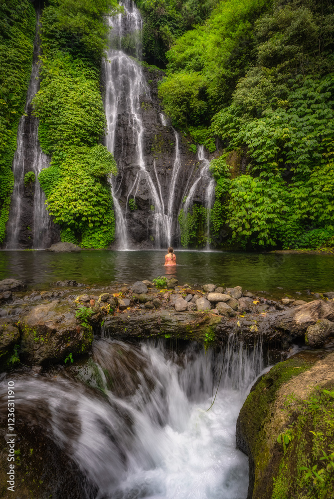 Obraz premium A Banyumala Twin Waterfalls gracefully cascades into a pristine, crystalclear pool, where girl relax, embraced by vibrant, lush foliage perfect escape into the serene beauty of nature, Bali, Indonesia