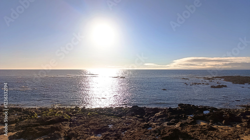 The ocean shore. The sun is shining brightly in the blue sky over the ocean. Horizontal image.