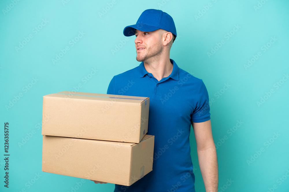 Delivery caucasian man isolated on blue background looking to the side Delivery caucasian man isolated on blue background looking to the side