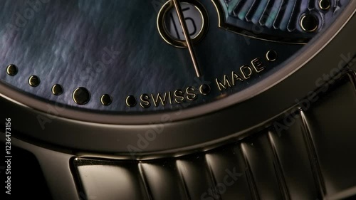 Zoom-in close-up of golden metallic luxury swiss women’s watch with deep blue nacre inlay and second arrow passing by the calendar. Light reveal the subject from the darkness