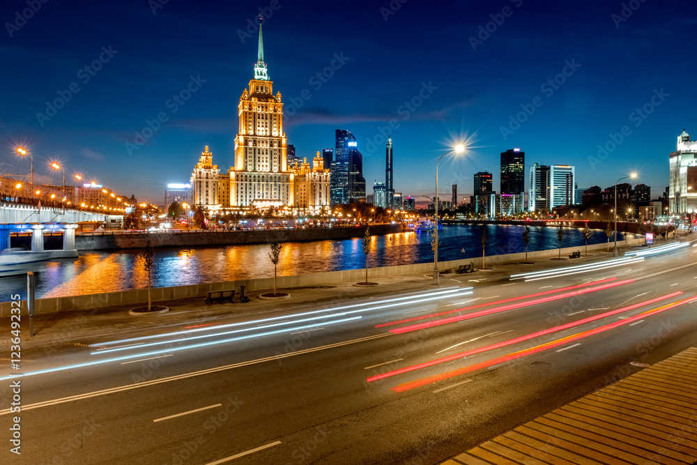 Obraz premium Illuminated high-rise stalinist building near river at summer night in Moscow, Russia. Historic name is Hotel Ukraina. Translation of the inscription on the facade: Ukraine