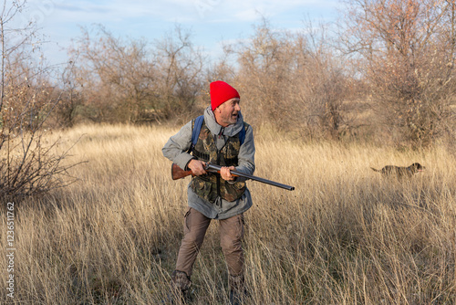 Mature hunter man holding a shotgun and walking through a field photo