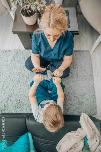boy sitting on carpet with therapist mirroring hand movements, alternative learning in friendly home environment, concept of special education and personal development. Top view