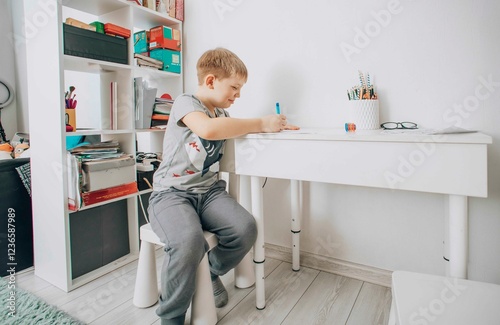 young boy focused on drawing at his study desk in a bright room, concept of early education, creativity in children, home schooling