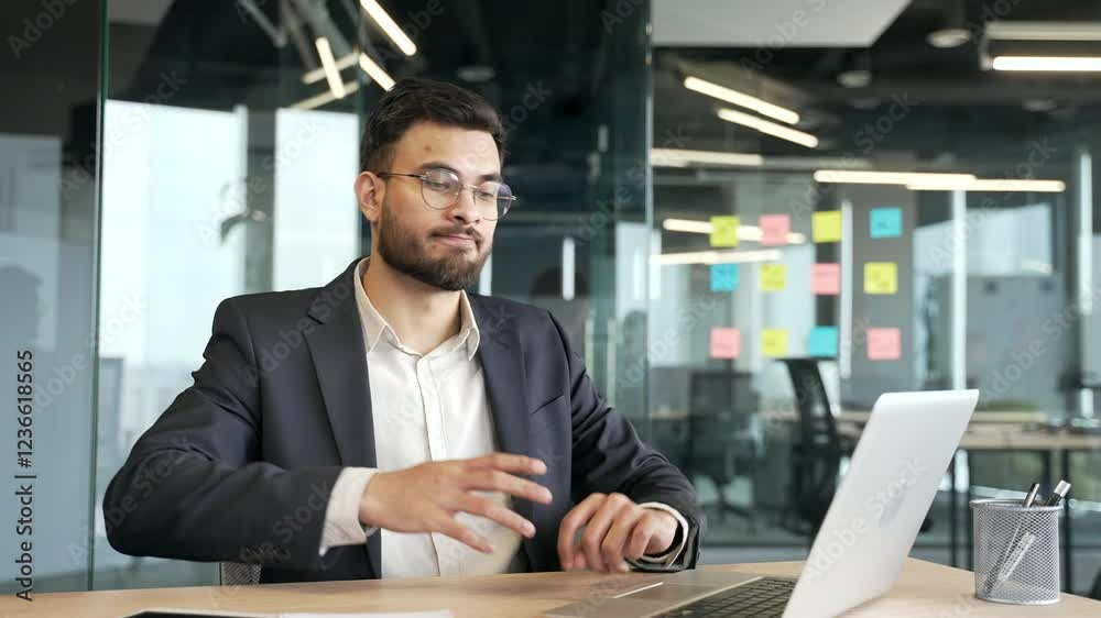 Happy businessman in a formal suit finished work on laptop while sitting at workplace in business office. Satisfied male worker puts his hands behind his head, stretches himself in chair. Work done