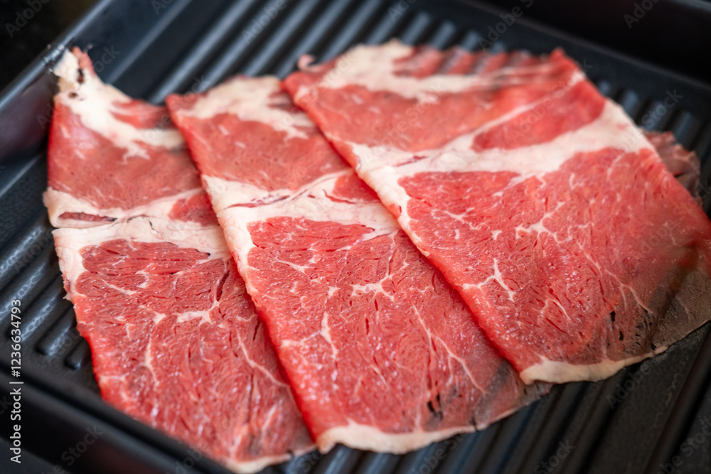 A close-up shot of sliced raw meat, arranged on a plate, ready to be cooked in a hot pot A close-up shot of sliced raw meat, arranged on a plate, ready to be cooked in a hot pot