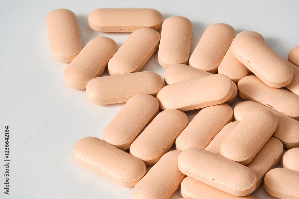 Numerous oval shaped pills creating a pile on a white surface, suggesting a medical or pharmaceutical concept Numerous oval shaped pills creating a pile on a white surface, suggesting a medical or pharmaceutical concept