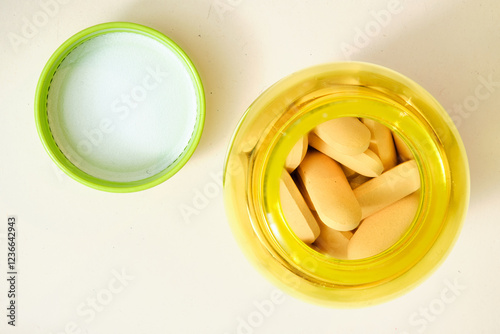 Yellow plastic bottle containing oblong pills with its green cap and foil seal removed, signifying health, wellness, or medical treatment photo