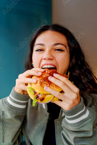 Foto Young woman taking a big bite of a burger in a restaurant, enjoying her meal