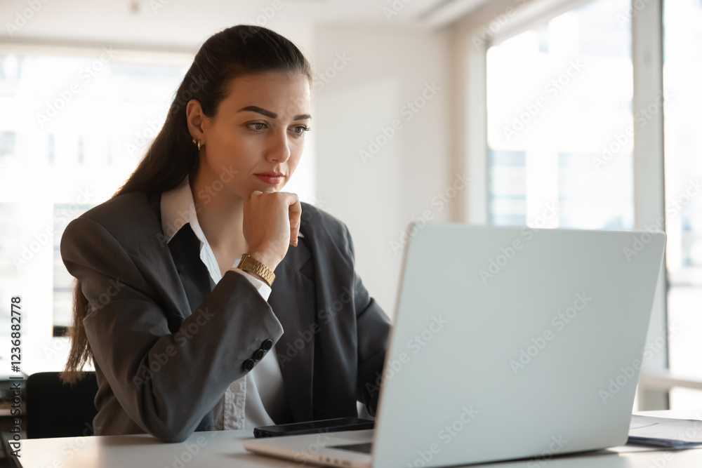 Focused pensive young businesswoman working at laptop in office, touching chin, thinking on online project, Internet marketing statistics, sitting at workplace table with desktop, using technology Focused pensive young businesswoman working at laptop in office, touching chin, thinking on online project, Internet marketing statistics, sitting at workplace table with desktop, using technology