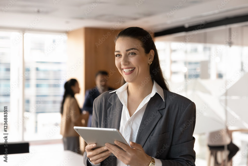 Happy positive young business leader woman looking away in office workspace, holding digital gadget, using tablet computer, thinking on successful Internet project, online sales growth