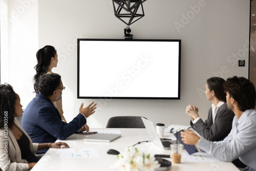 Diverse business team of colleagues meeting at table offline, looking at blank large wall screen with copy space for video conference chat or webinar interface, using online communication technology