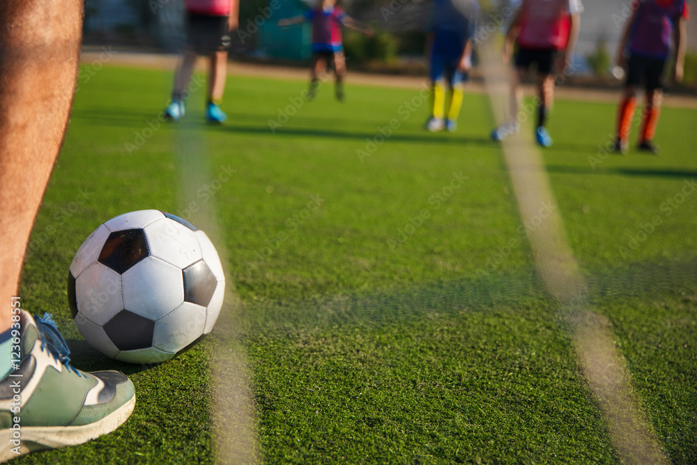 A close-up view of a soccer ball on a green field, with a player’s foot preparing to kick it. In the background, other players in colorful jerseys are seen practicing, with a clear blue sky. A close-up view of a soccer ball on a green field, with a player’s foot preparing to kick it. In the background, other players in colorful jerseys are seen practicing, with a clear blue sky.