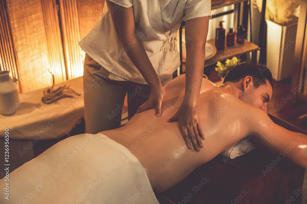 Fototapeta premium Caucasian man customer enjoying relaxing anti-stress spa massage and pampering with beauty skin recreation leisure in warm candle lighting ambient salon spa at luxury resort or hotel. Quiescent