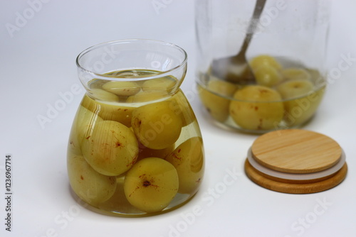 Brine pickled Indian gooseberries in glass bottle, surrounded by fresh gooseberries