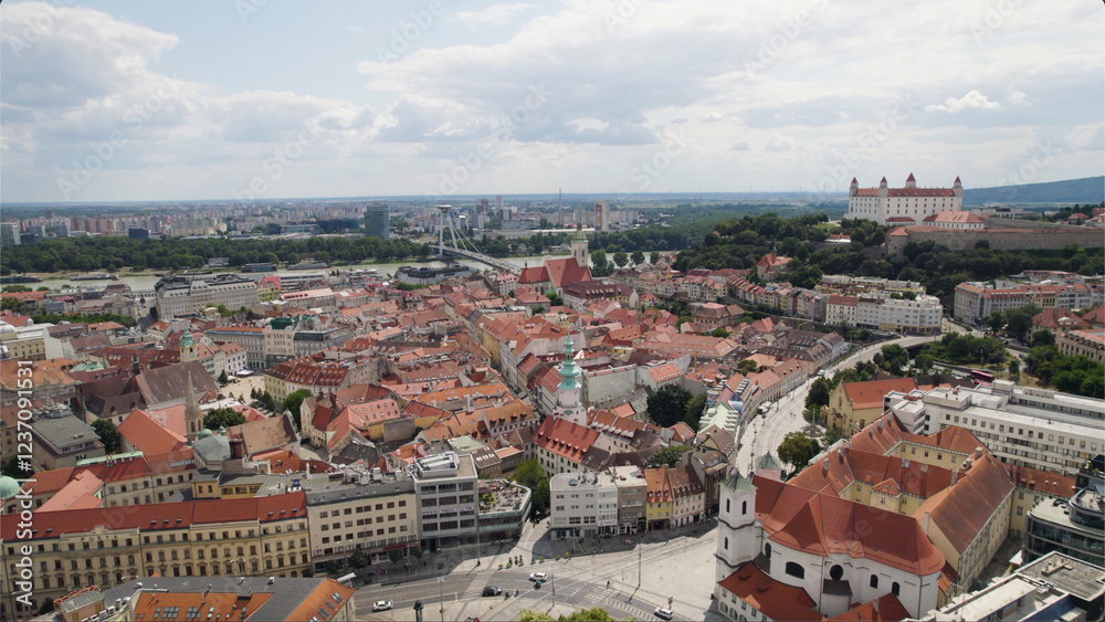 Obraz premium Bratislava city with red-roofed buildings, historic castle, and cloudy sky, aerial view