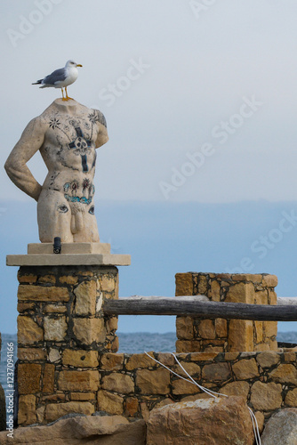 Varna, Bulgaria -12.10.2023: A seagull perched on a headless statue built on a wall of stones. The seagull represents the head of the statue. Abstract painting. photo