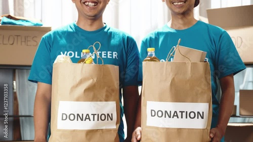 Happy teenage volunteers holding food bags and smiling at the camera in a charity setting. Committed to making a difference in their community through donations. Food donations, charity activities