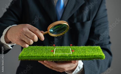 A businessman examines a plot of land with a magnifying glass. Purchase and sale of land. Plot valuation. Checking for arrests and possible risks to the successful conclusion of the contract.
