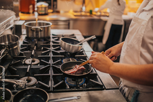 A skilled chef is diligently cooking various types of meat in a frying pan that is placed on top of a stove, creating delicious dishes