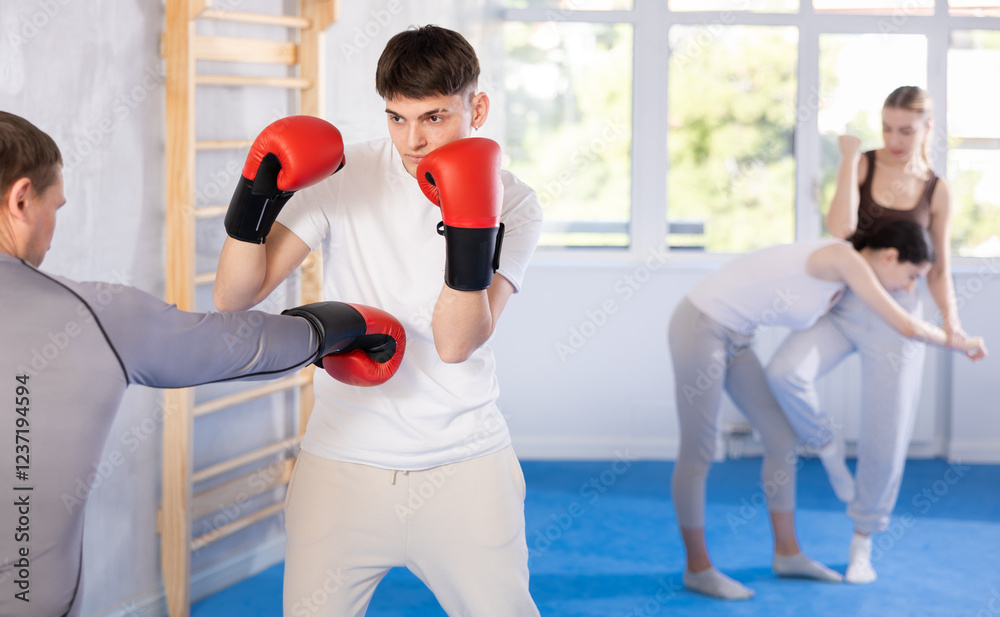 Young guy and adult man in boxing gloves training boxing punches in studio.. Young guy and adult man in boxing gloves training boxing punches in studio..