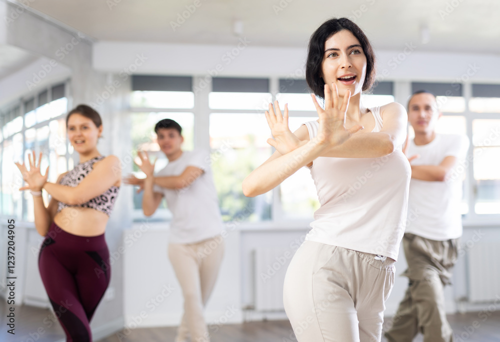 Fototapeta premium Happy emotional sporty young female dancer rehearsing popping techniques during group workout in modern street dance studio