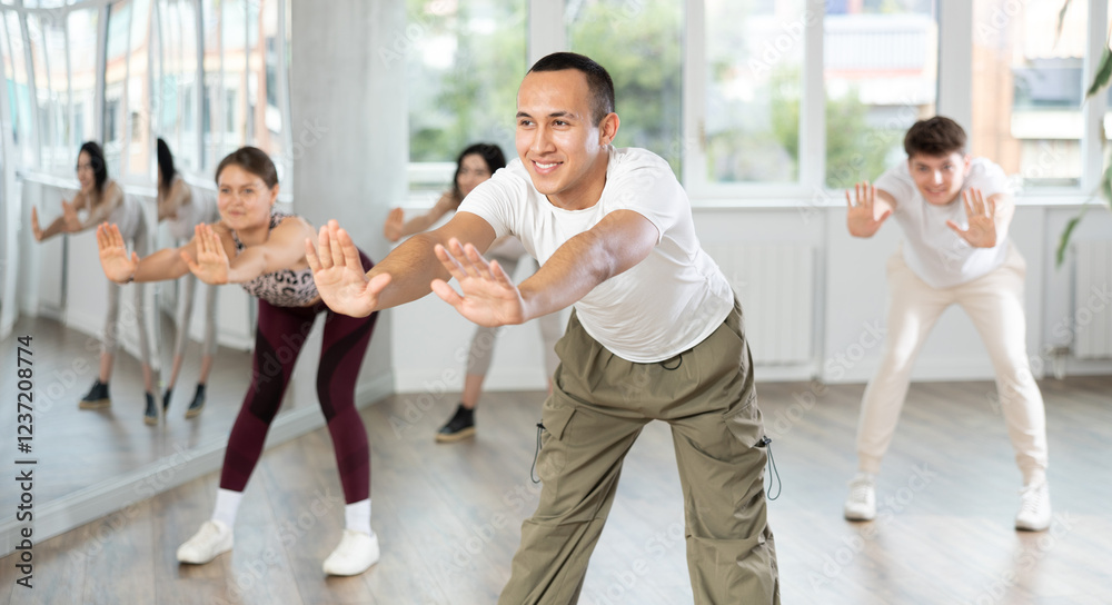 Naklejka premium Young guy enjoys dancing, learning to twerk during group class at studio school for young people. Devotion of modern trend pastime, active lifestyle and hobbies
