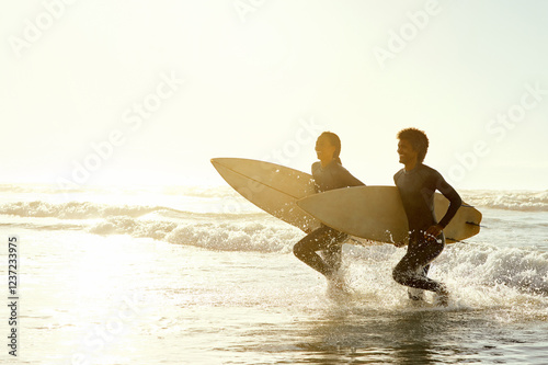 Vászonkép Travel, sunset and couple running on the beach with surfboards to practice surfing while on vacation