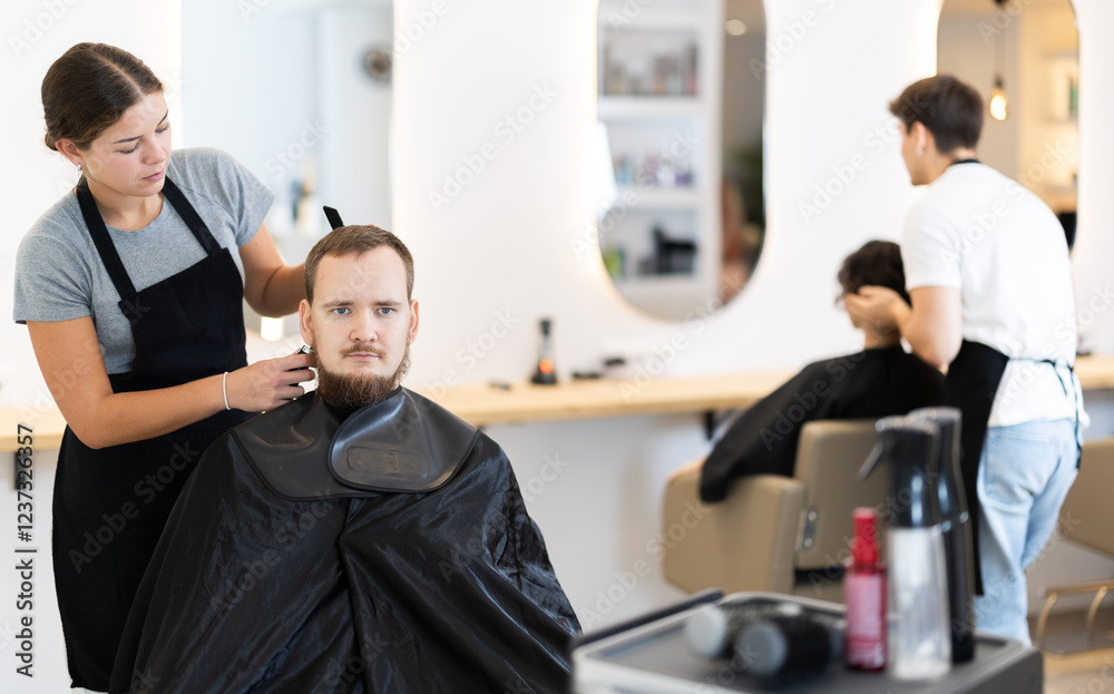 During visit to barbershop, male client communicate with girl stylist, ask to perform haircut, shortening of hair. Hairdresser and visitor discuss hairstyle, master explains and assumes final result During visit to barbershop, male client communicate with girl stylist, ask to perform haircut, shortening of hair. Hairdresser and visitor discuss hairstyle, master explains and assumes final result