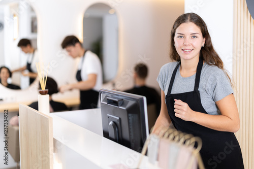 Young female hairdresser stylist stands at cash register in beauty salon photo