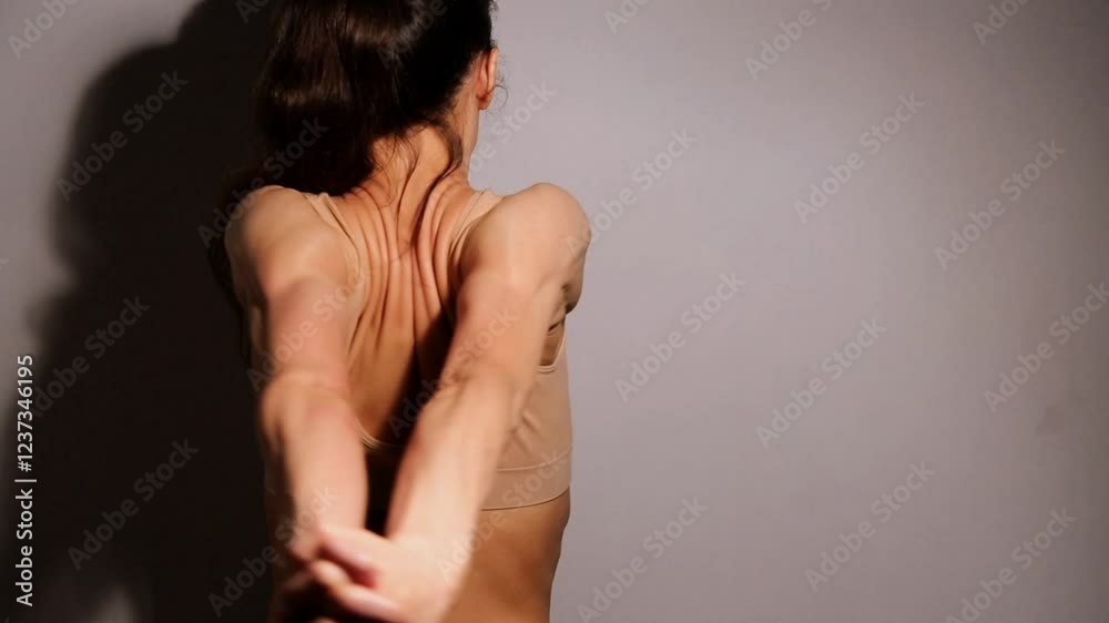 Sport woman doing stratching exercises for shoulders, scapula and healthy upper back, holds hands in a lock and moves hands from side to side. Female model in bra on studio low key shadow. Back view Sport woman doing stratching exercises for shoulders, scapula and healthy upper back, holds hands in a lock and moves hands from side to side. Female model in bra on studio low key shadow. Back view