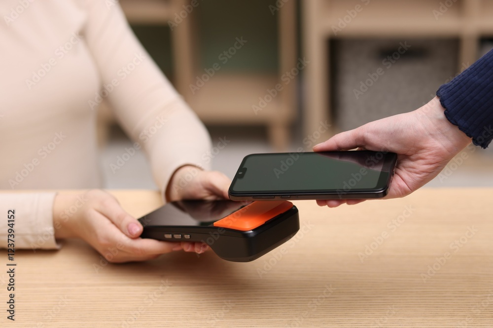 Woman paying with smartphone via terminal at wooden counter indoors, closeup Woman paying with smartphone via terminal at wooden counter indoors, closeup