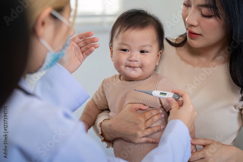 Pediatrician checking baby temperature with thermometer in clinic. photo