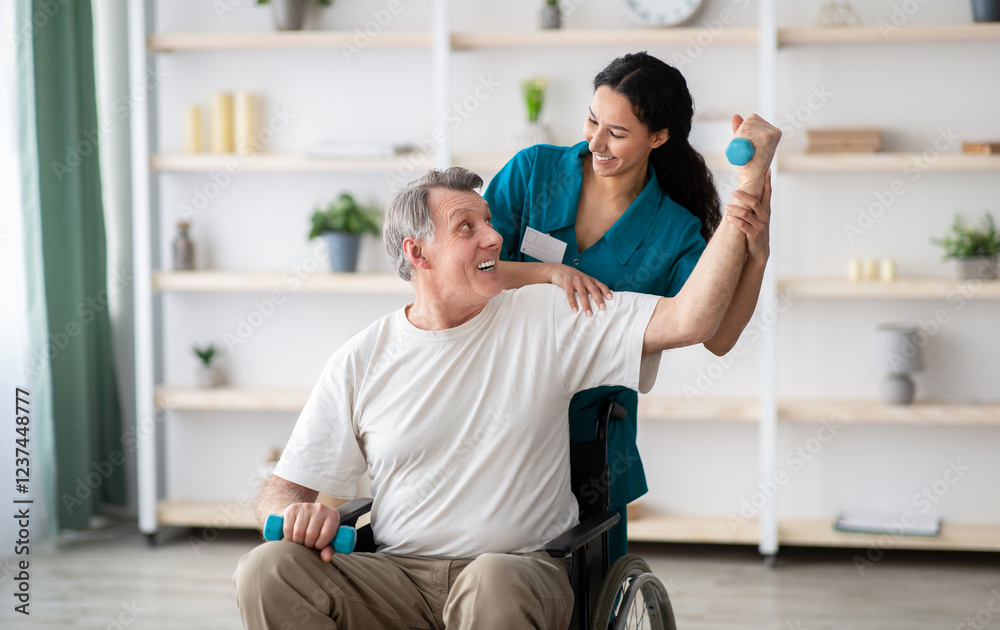Obraz premium Rehabilitation of disabled people concept. Young physiotherapist helping senior male patient in wheelchair exercise at home. Handicapped elderly man training with dumbbells