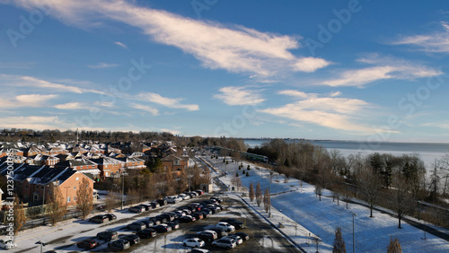 Snowy suburban neighborhood overlooks a winter lake. Tranquil scene with parked cars and a train.