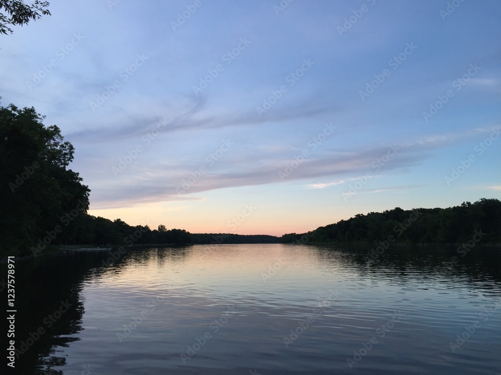 Subtle blue and orange sunset reflecting on lake water. A summer scene with clouds and treeline Subtle blue and orange sunset reflecting on lake water. A summer scene with clouds and treeline
