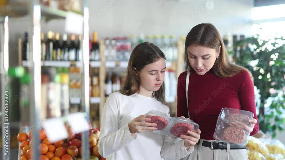 Happy teen girl and her mom deciding between beef burger in supermarket Happy teen girl and her mom deciding between beef burger in supermarket